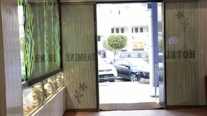 A hotel entrance with a glass display case filled with items, a view of parked cars outside, and a door with a floral design. - Hotel Yasmine (Sfax)