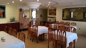 A dining area with multiple tables and chairs, a kitchen area in the background, and a mirror on the wall. - Hotel Yasmine (Sfax)