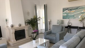 A modern living room with a fireplace, grey sofas, a coffee table, and a painting on the wall. - VILLA on a golf course close to the beach, swimming pool 50 metres away, WIFI fibre.  (BUDENS)