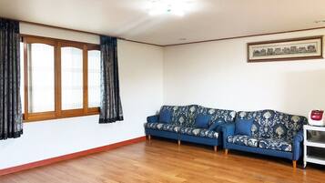 A living room with a blue patterned sofa, wooden flooring, a window with curtains, and a framed picture on the wall.