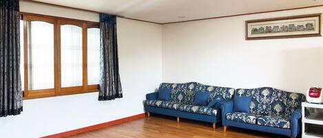 A living room with a blue patterned sofa, wooden flooring, a window with curtains, and a framed picture on the wall.