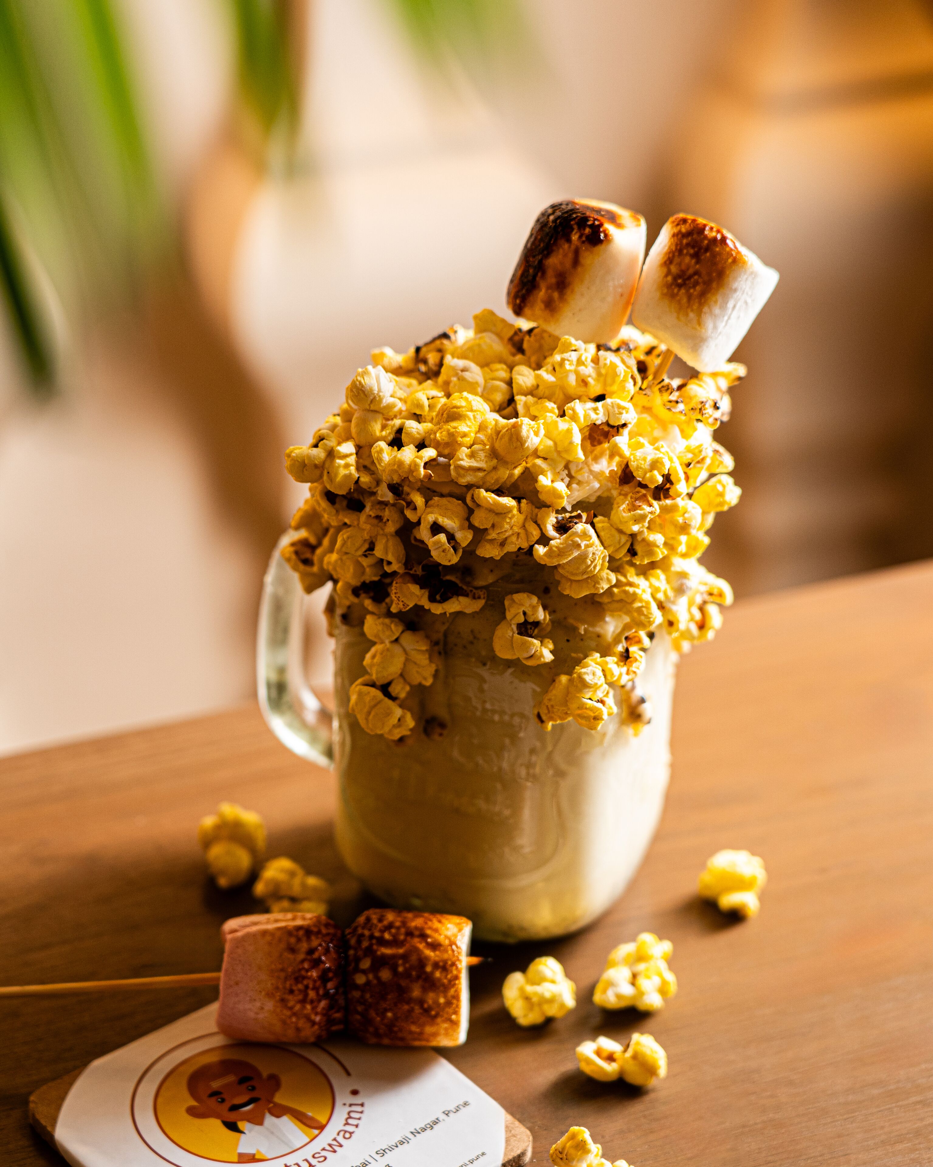 A glass mug filled with popcorn and marshmallows on a wooden table.