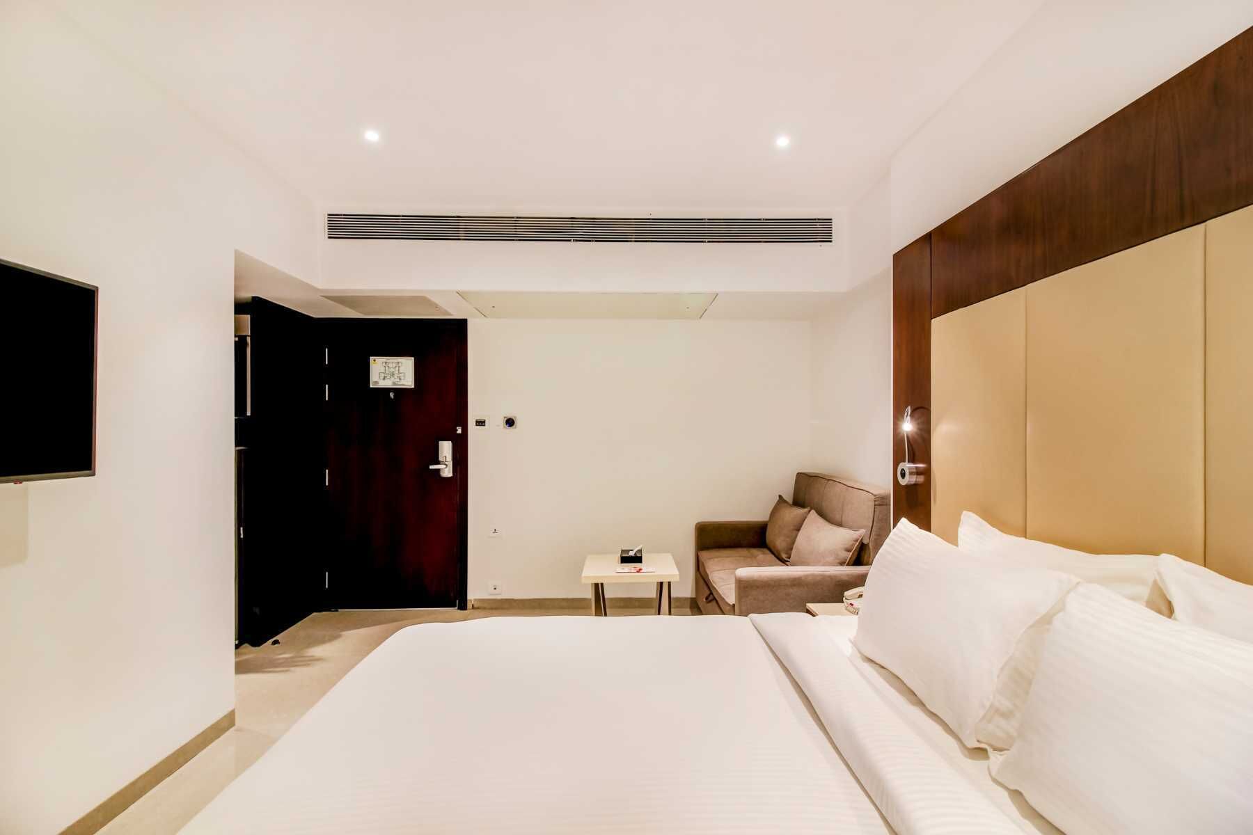 Une chambre d’hôtel avec un grand lit, une petite table, un canapé et un téléviseur fixé au mur.