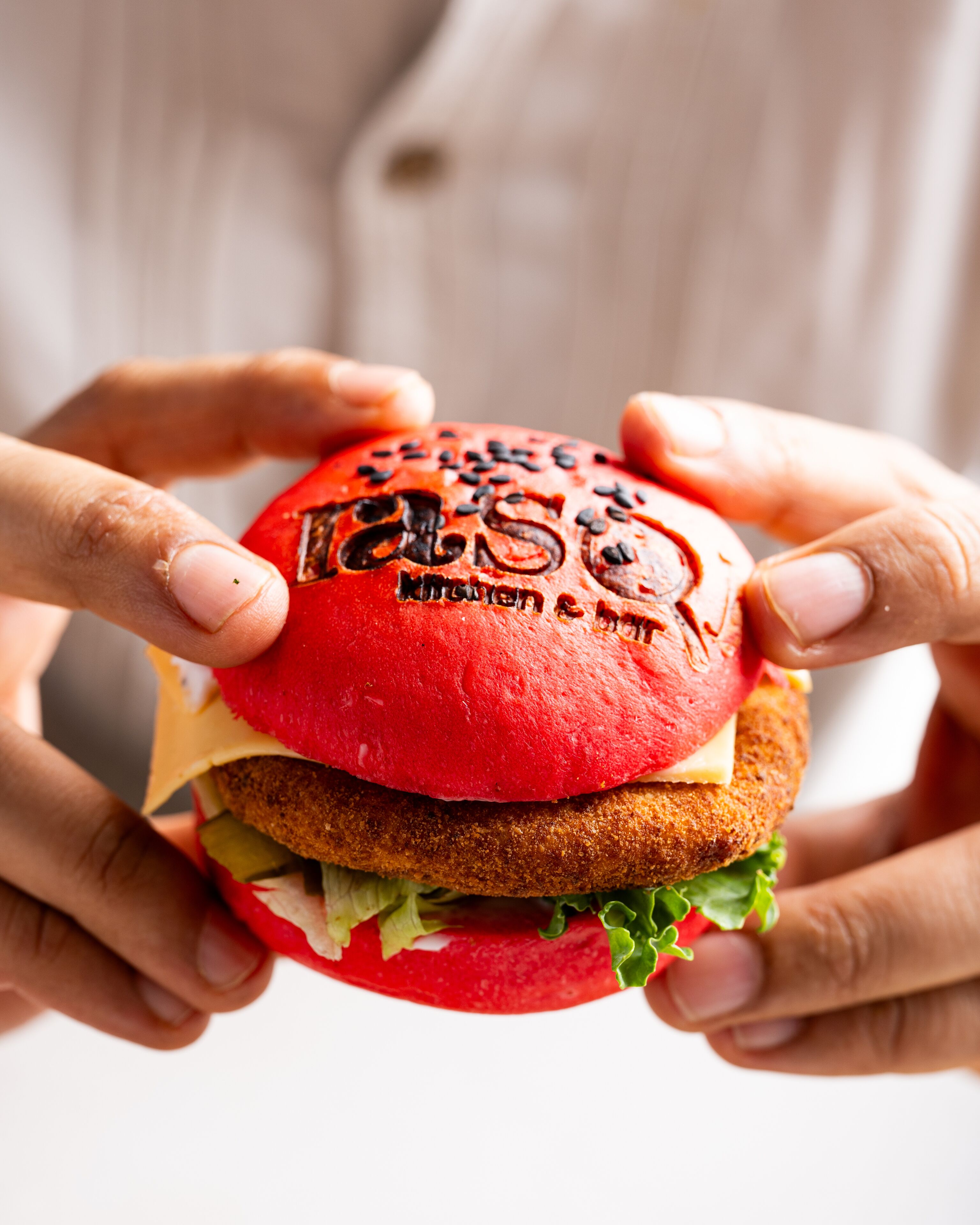A person holding a burger with a red bun and a visible logo.