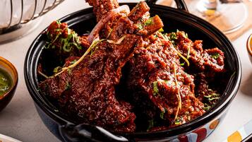 A bowl of spicy chicken wings garnished with herbs, a glass of orange juice, and a plate of fried food.