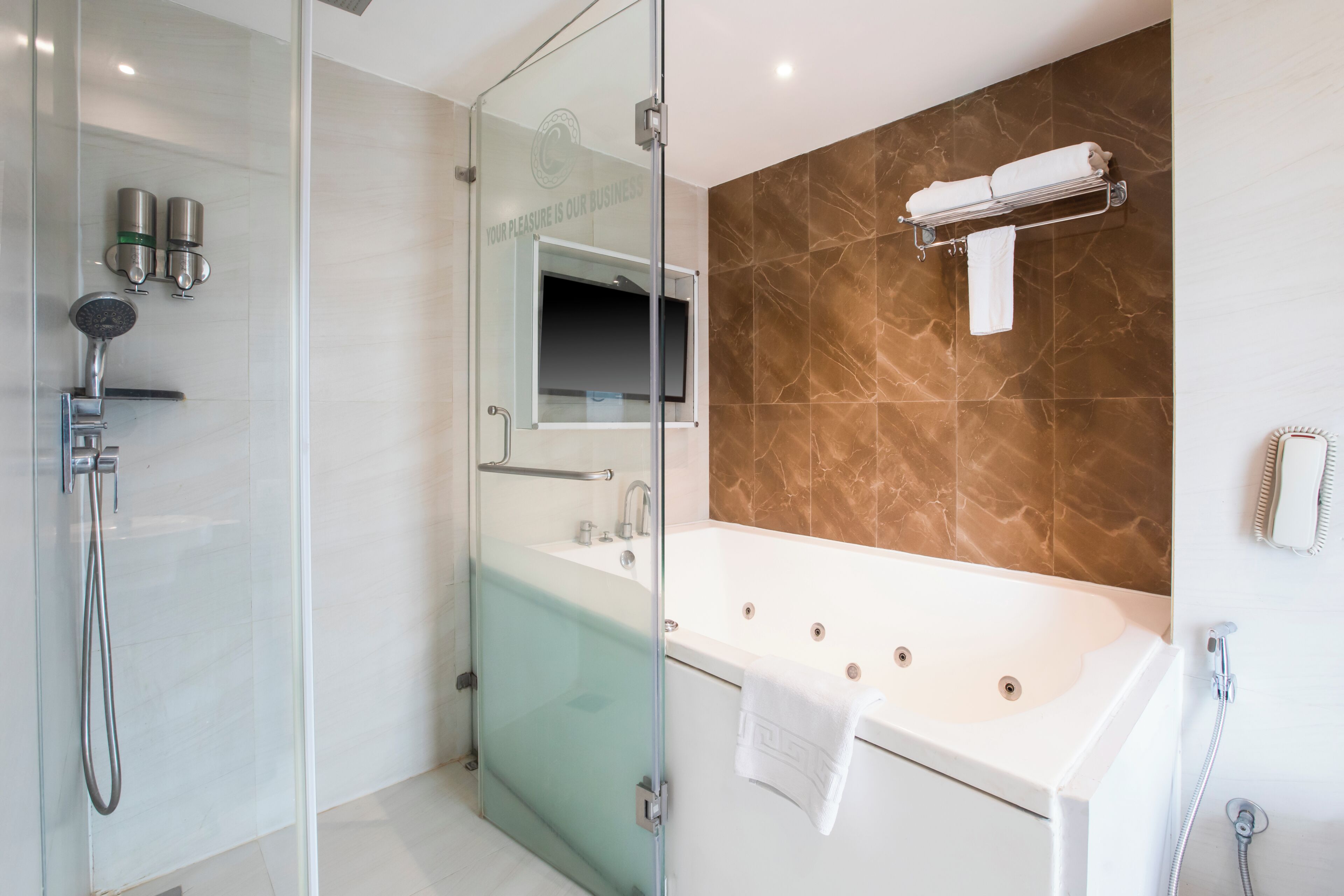 A modern bathroom with a glass-enclosed shower, a large bathtub, and a marble-tiled wall.
