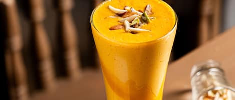Un vaso alto de batido de naranja con nueces encima, sobre una mesa de madera con un posavasos.