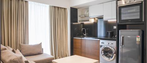Un espacio habitable pequeño con sofá, una mesita, lavadora y refrigerador.