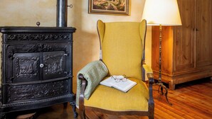 Une pièce avec un poêle ancien, un fauteuil vert, un meuble en bois et une lampe.