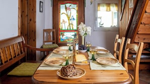 Une table de salle à manger en bois, mise avec des assiettes, des verres et une bouteille de vin, entourée de chaises et d’un banc, tous en bois.