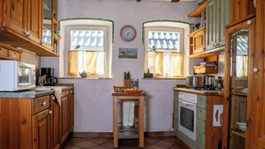 Une cuisine de taille réduite, dotée de meubles en bois, d’un four à micro-ondes, d’une cuisinière et de deux fenêtres avec des rideaux.