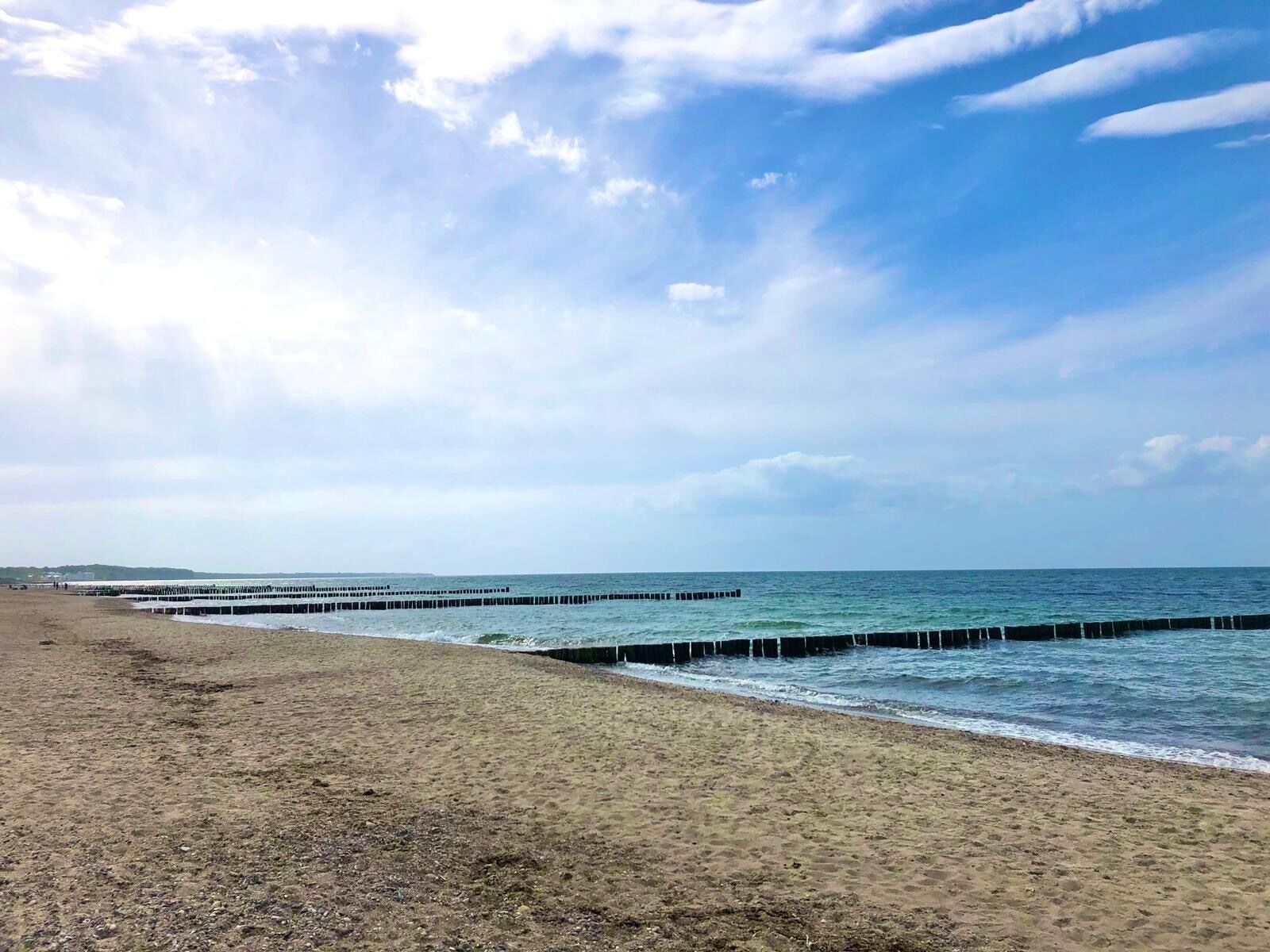 Ein Strand mit einer langen Seebrücke, sandigem Ufer und einem teilweise bewölkten Himmel.