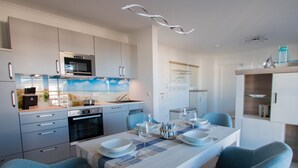A modern kitchen with a dining area, featuring a large island, built-in appliances, and a view of the beach through the window. - Apartment beach life. 2 bedrooms, high quality furnishings, great sea views! (Börgerende-Rethwisch)