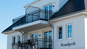 A multi-story building with balconies, a sign reading "Strandperle," and a number "28" on the facade. - Apartment beach life. 2 bedrooms, high quality furnishings, great sea views! (Börgerende-Rethwisch)
