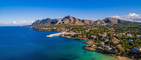 Une ville côtière offrant une vue dégagée sur la mer, avec une petite plage et une chaîne de montagnes en arrière-plan.