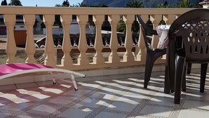 Un balcon doté d’un sol carrelé, d’une balustrade blanche et offrant une vue sur des montagnes en arrière-plan.