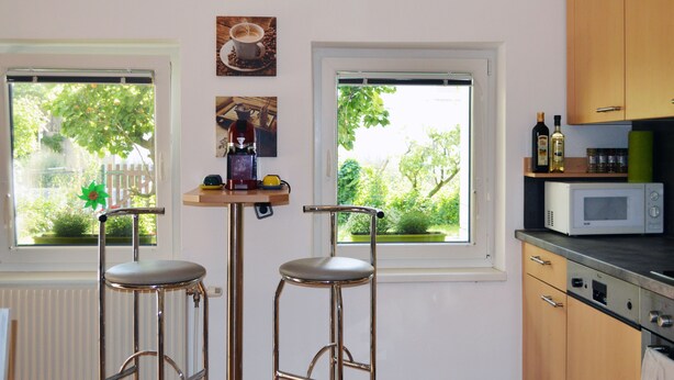Una cocina con dos taburetes de bar, un microondas y un reloj en la pared.