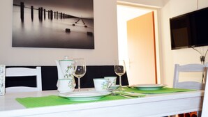 Una mesa de comedor dispuesta con platos, vasos y cubiertos, un cuadro en la pared superior y un televisor en la pared.