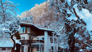 A multi-story house with a balcony, surrounded by snow-covered trees.