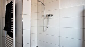 En dusch med ett duschmunstycke som kan hållas i handen och en väggmonterad blandare i ett badrum med kakel.