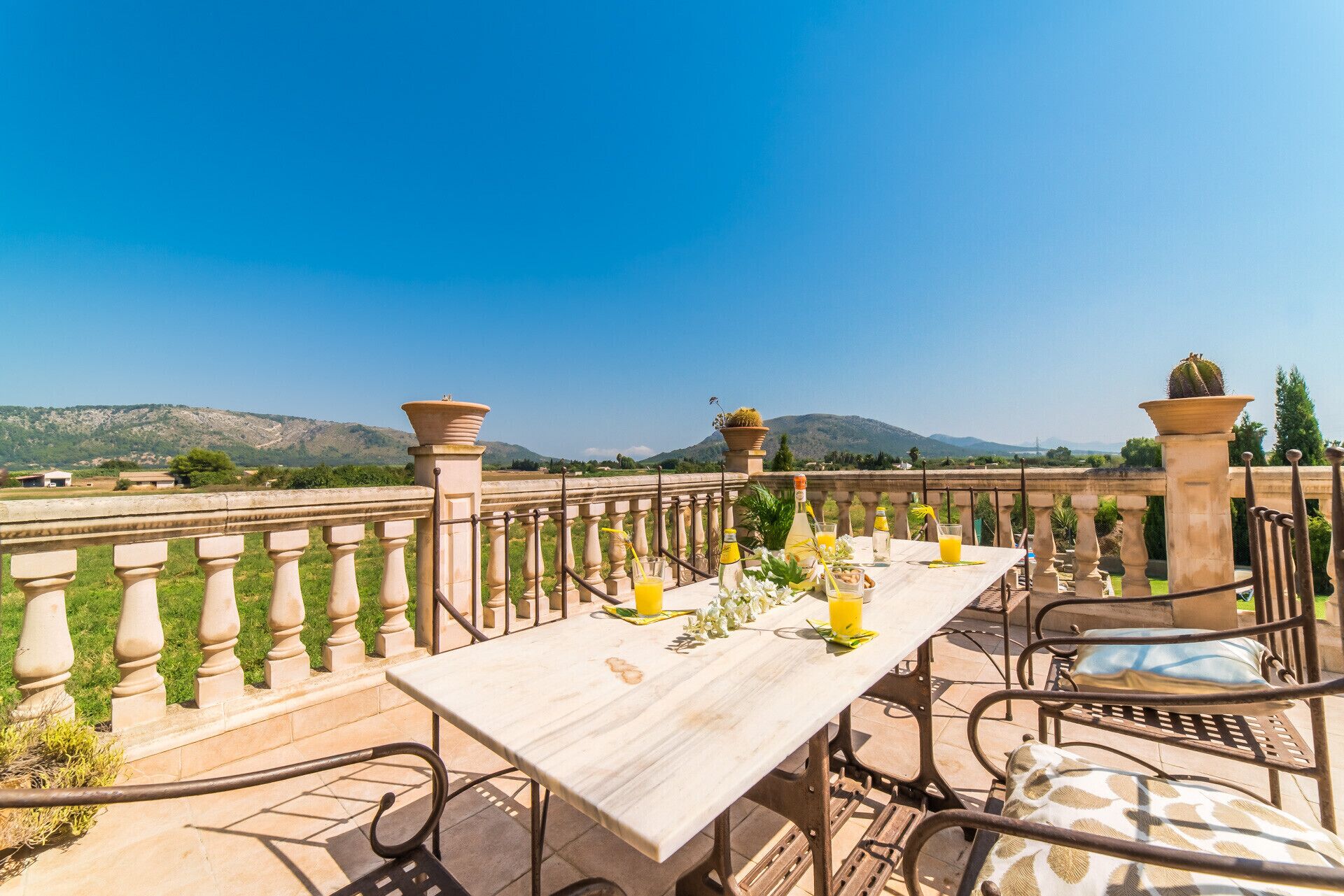An outdoor dining area with a table set for two, a view of the countryside, and a clear blue sky.
