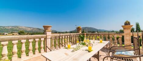 An outdoor dining area with a table set for two, a view of the countryside, and a clear blue sky.