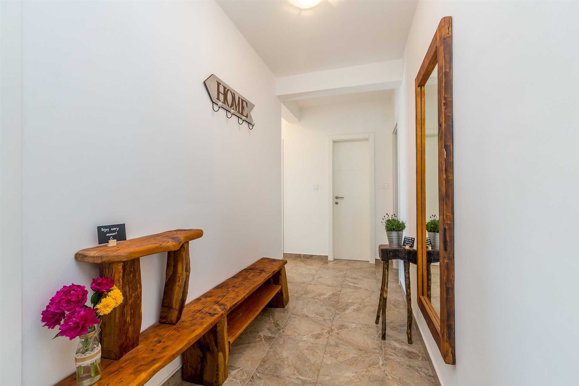 A hallway with a wooden bench, a 'HOME' sign, a mirror, and potted plants.