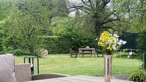 An outdoor seating area with wicker furniture and a table, surrounded by a lush garden and a large tree. - Farmhouse from 1869 with modern ambience, free WLAN, oven and large garden (Dahlem- Berk)