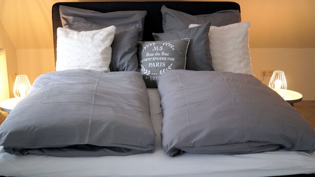 A neatly made bed with grey bedding and a decorative pillow with text. - Farmhouse from 1869 with modern ambience, free WLAN, oven and large garden (Dahlem- Berk)