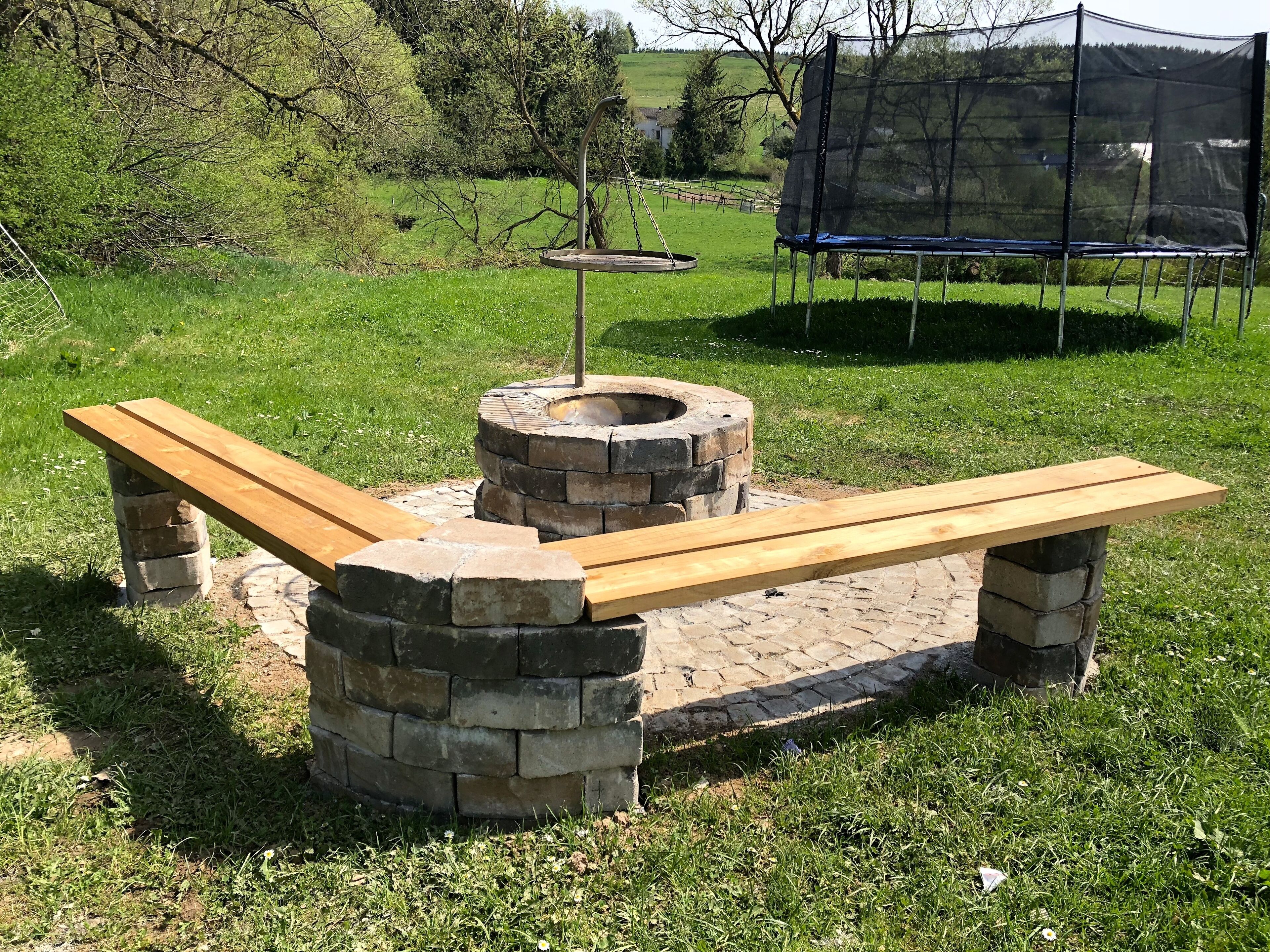 A stone fire pit with benches, surrounded by grass and trees.