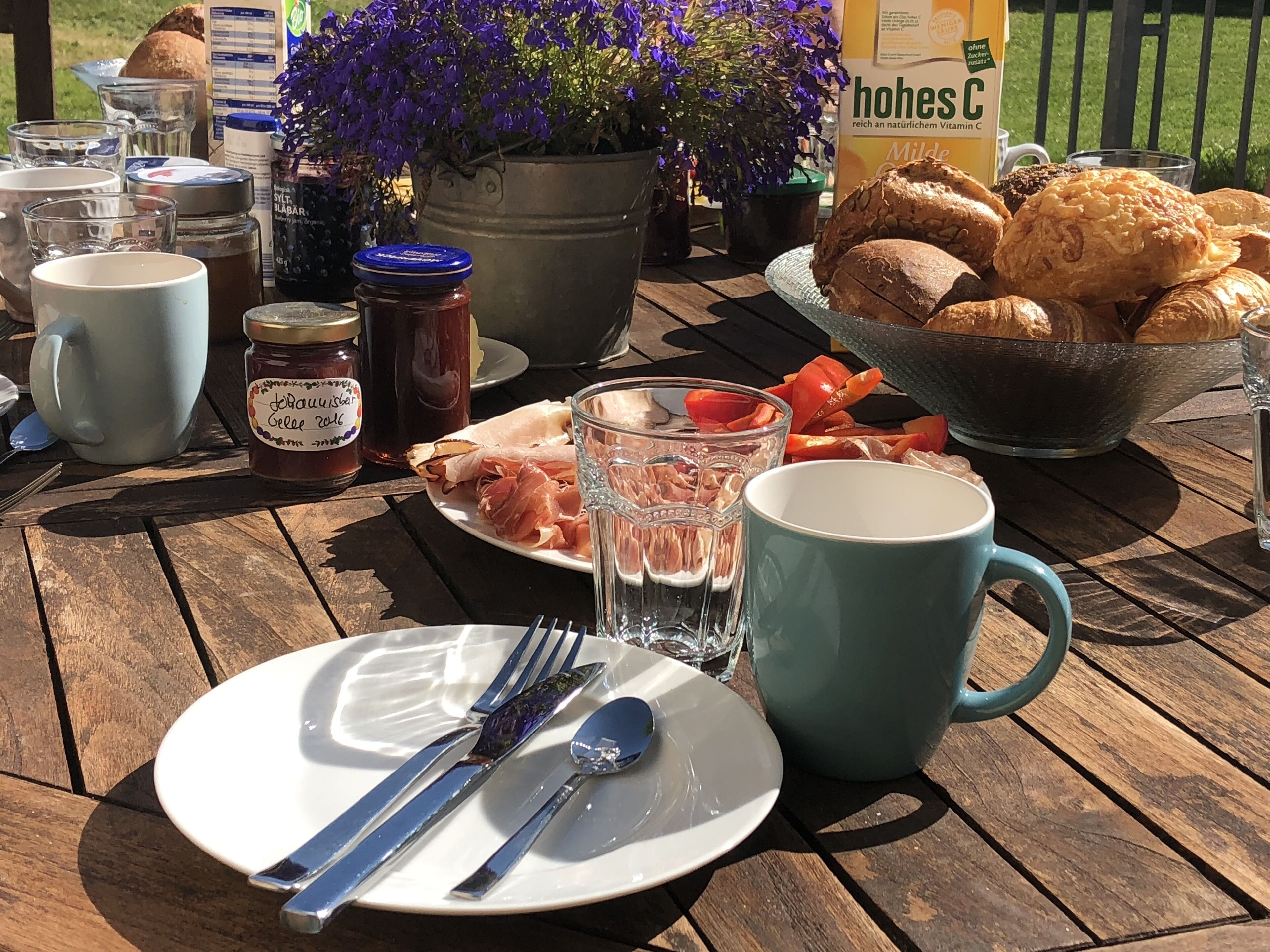 Een houten tafel gedekt met een bord eten, een potje jam, een glas water en een mok.
