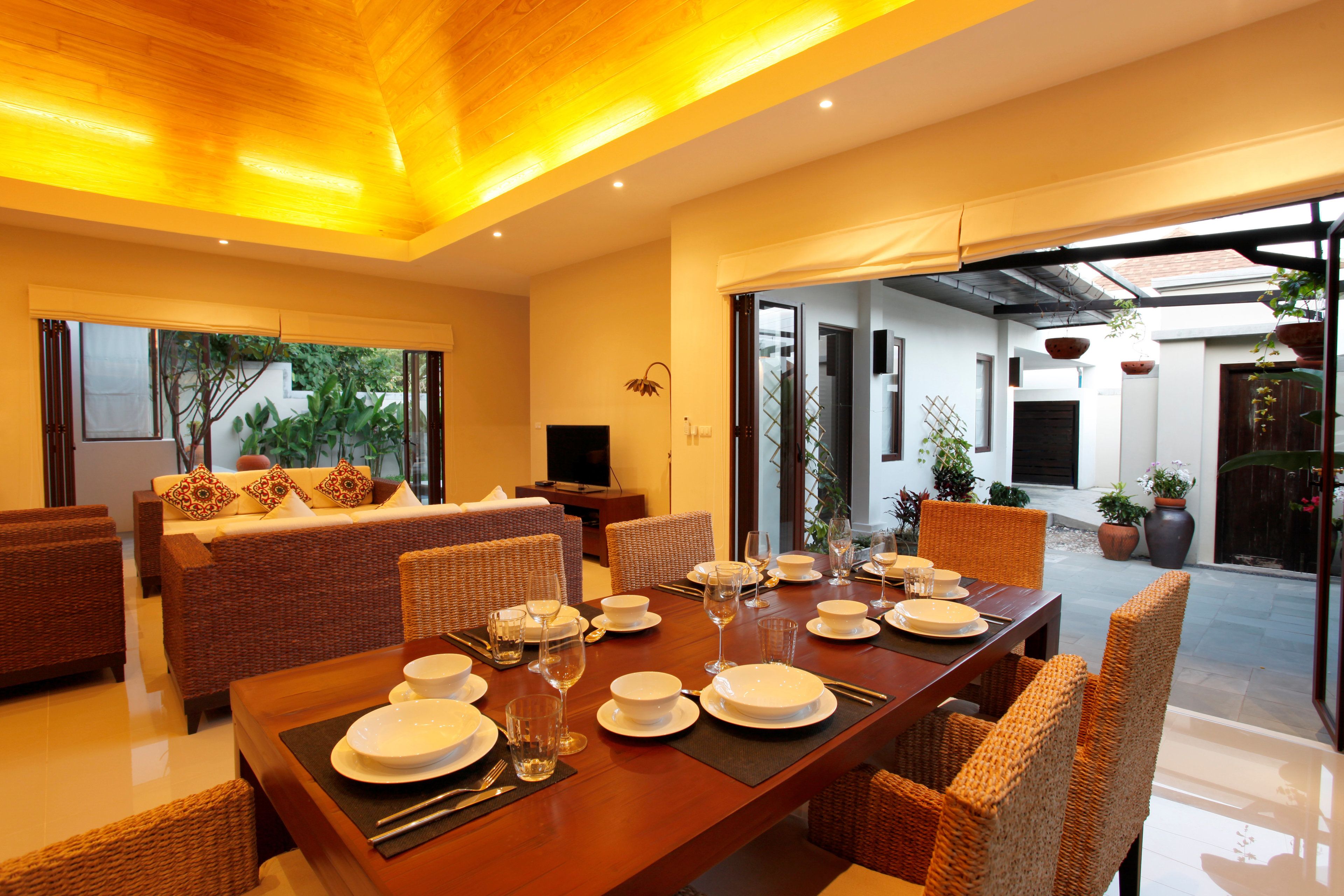 A modern dining area with a wooden table set for a meal, wicker furniture, and a view of the outdoor patio.