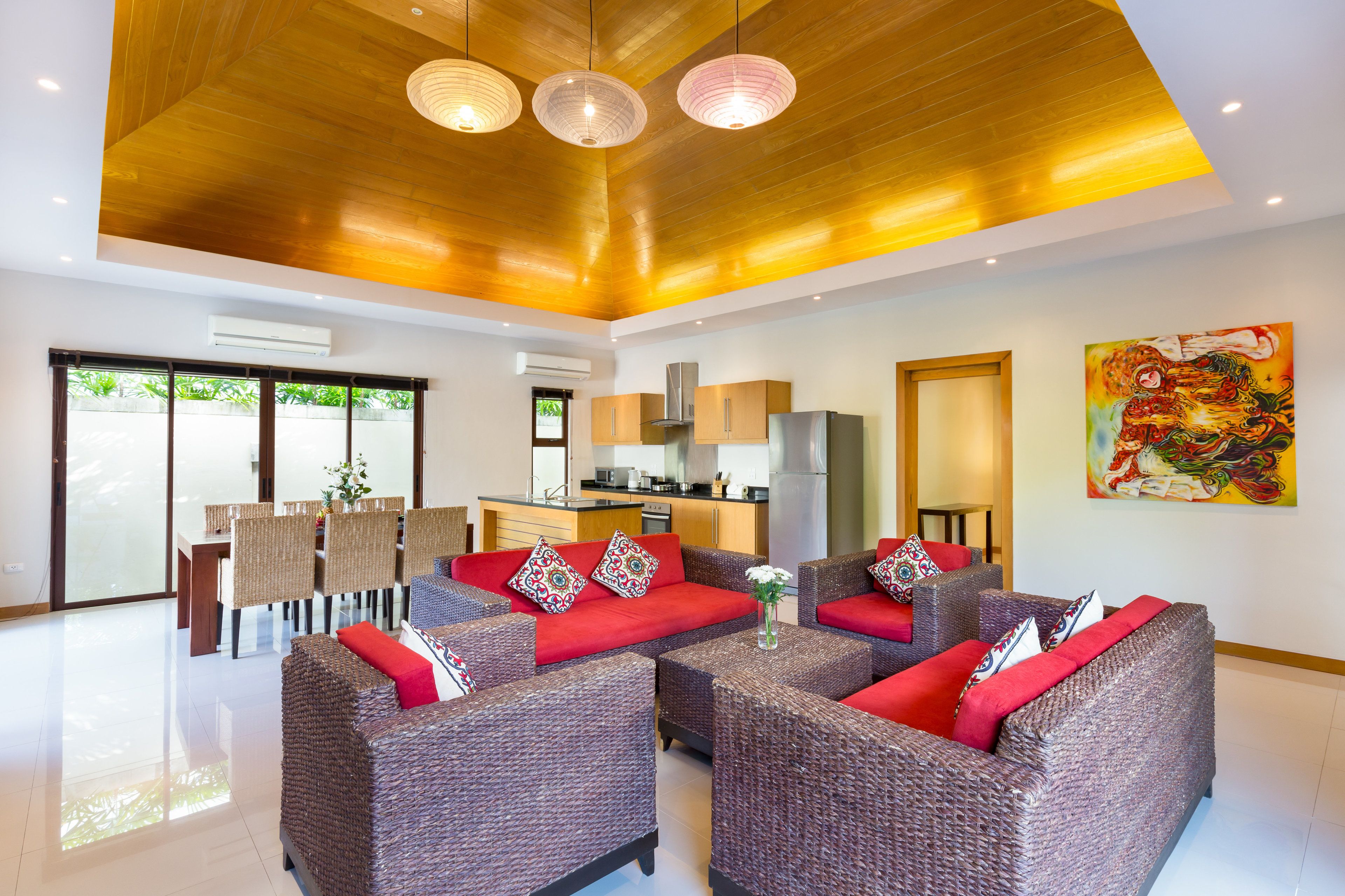 A spacious living area with wicker sofas, a dining table, and a kitchen in the background.