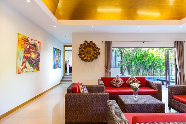 Un salon moderne avec des meubles en osier, des coussins rouges et une grande décoration murale en forme de soleil rayonnant.