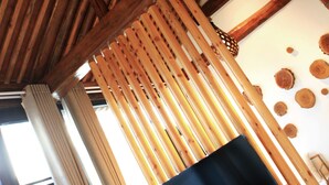 A room with wooden beams, a hanging light fixture, a TV mounted on a wooden panel, and a window with curtains. - Carpenter's Rustic Courtyard-Great Wall (Huairou)