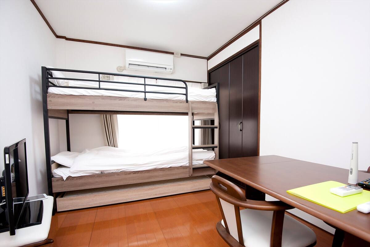 Ein Stockbett mit Schreibtisch, Stuhl, Kleiderschrank und Fernseher.