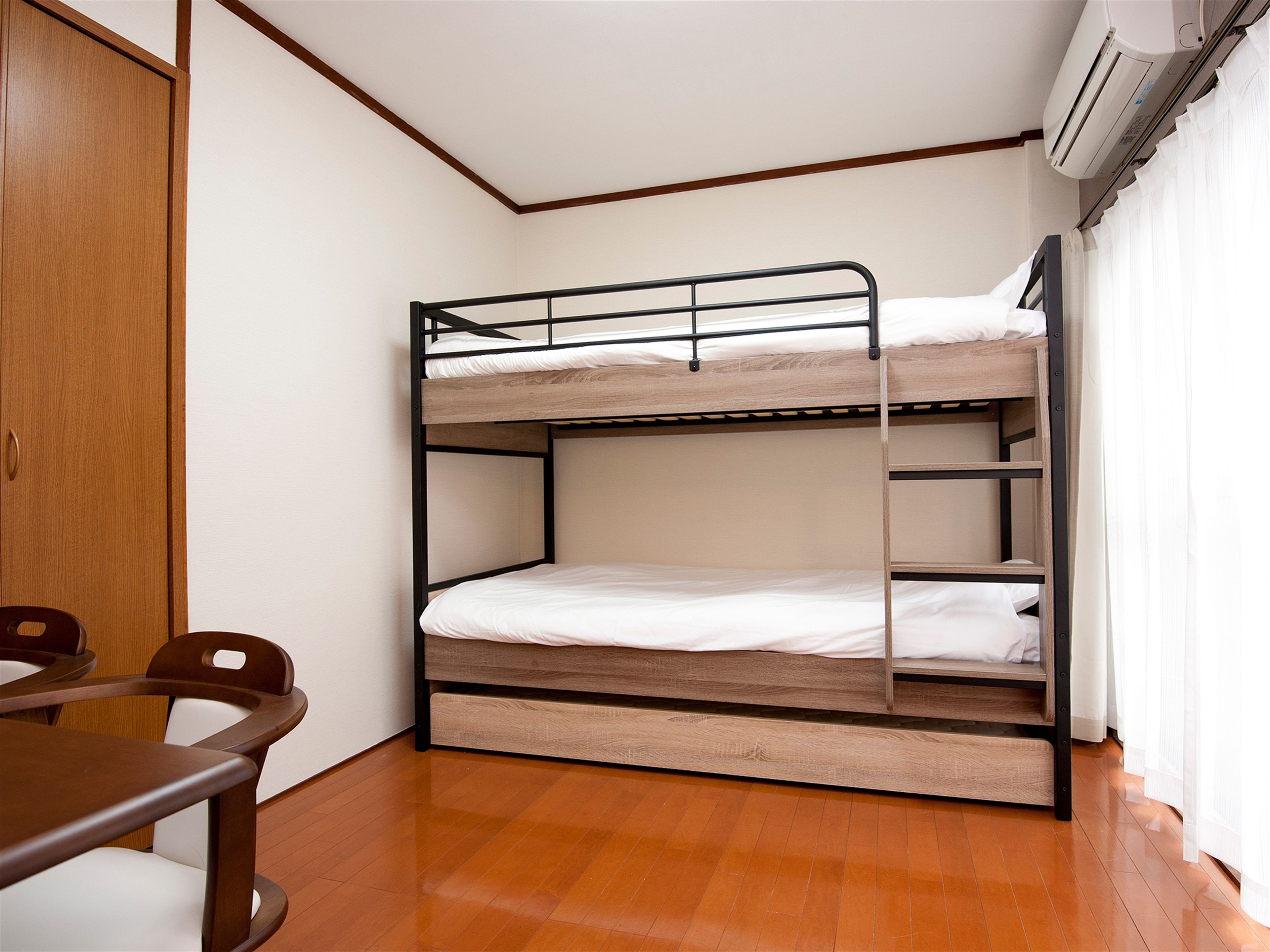 Une chambre avec un lit superposé, un plancher en bois, un bureau et une chaise.