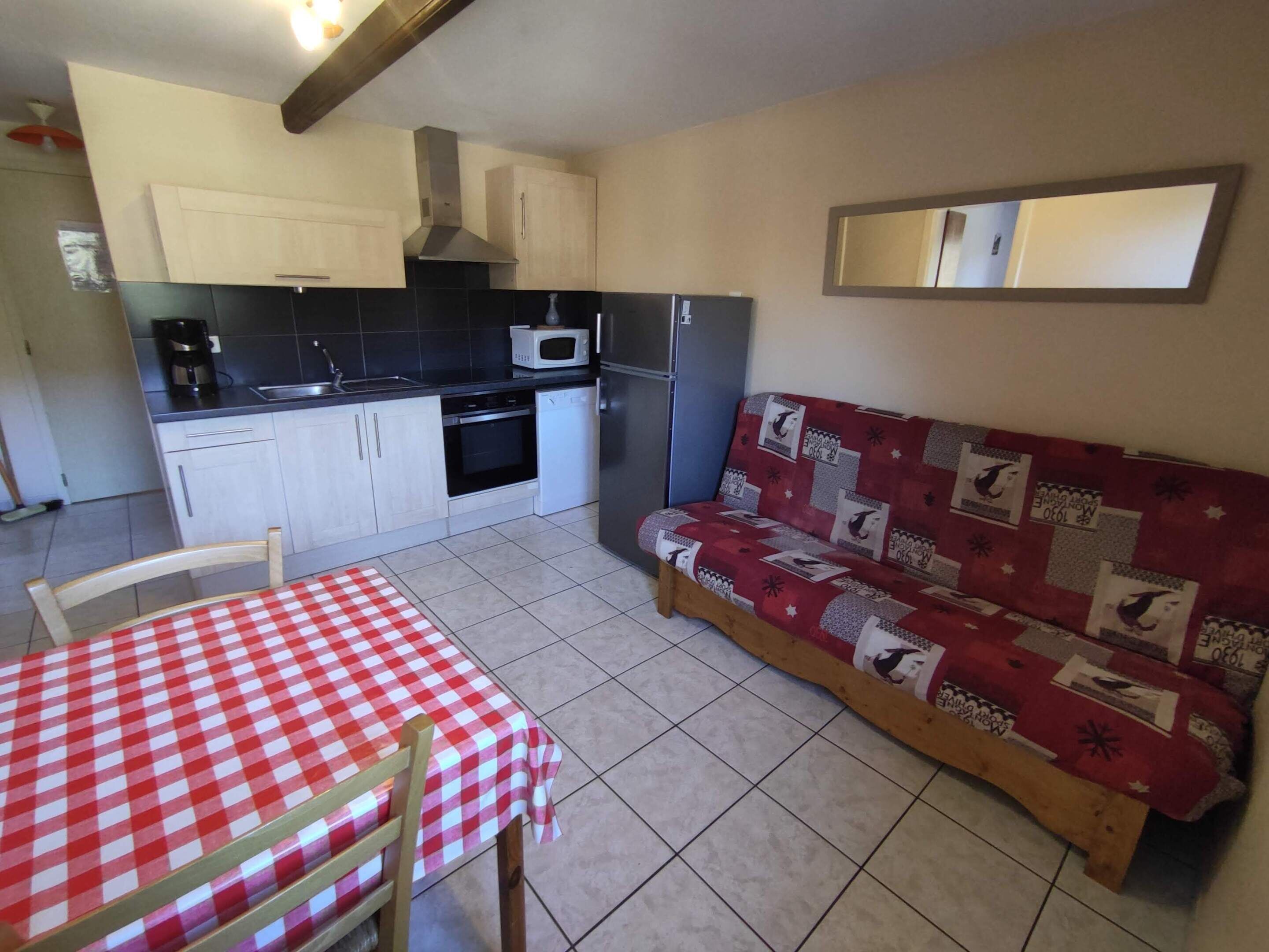 A compact kitchen with a dining area, including a checkered table, chairs, and a sofa with patterned upholstery.