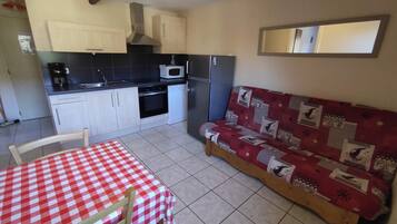 A compact kitchen with a dining area, including a checkered table, chairs, and a sofa with patterned upholstery.