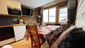 A cozy kitchen with wooden cabinets, a built-in oven, and a dining area with a table covered in a quilt. - 3 BEDROOMS, COCOONING, CENTER, CHALET STYLE, WELLNESS (Morzine)