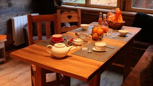 A wooden dining table set with a teapot, cups, and oranges, with a TV in the background and a view of the outdoors through large windows. - 3 BEDROOMS, COCOONING, CENTER, CHALET STYLE, WELLNESS (Morzine)