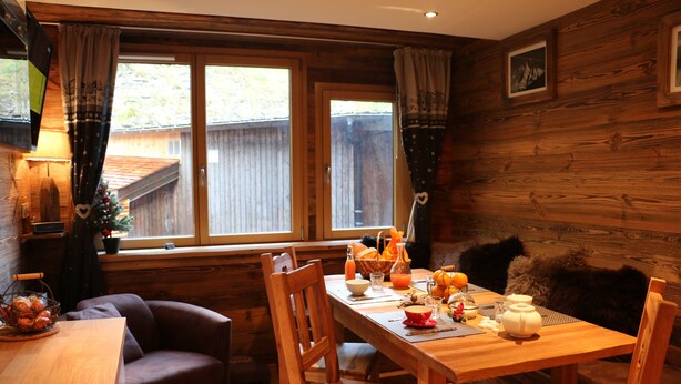 A cozy dining area with a wooden table set for two, a brown sofa, and a window with curtains. - 3 BEDROOMS, COCOONING, CENTER, CHALET STYLE, WELLNESS (Morzine)
