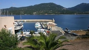 Uma marina com barcos atracados, um pequeno edifício e uma montanha ao fundo.