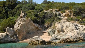 Uma praia rochosa com águas turquesa cristalinas, cercada por vegetação verde exuberante.