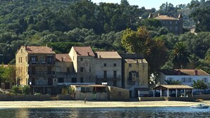 Um edifício costeiro com telhado em cerâmica, localizado ao lado de uma praia arenosa e de um corpo de água.