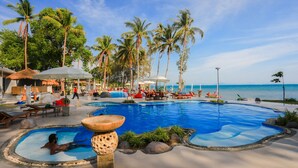 Un espace piscine aménagé avec des chaises longues, des parasols et des palmiers.