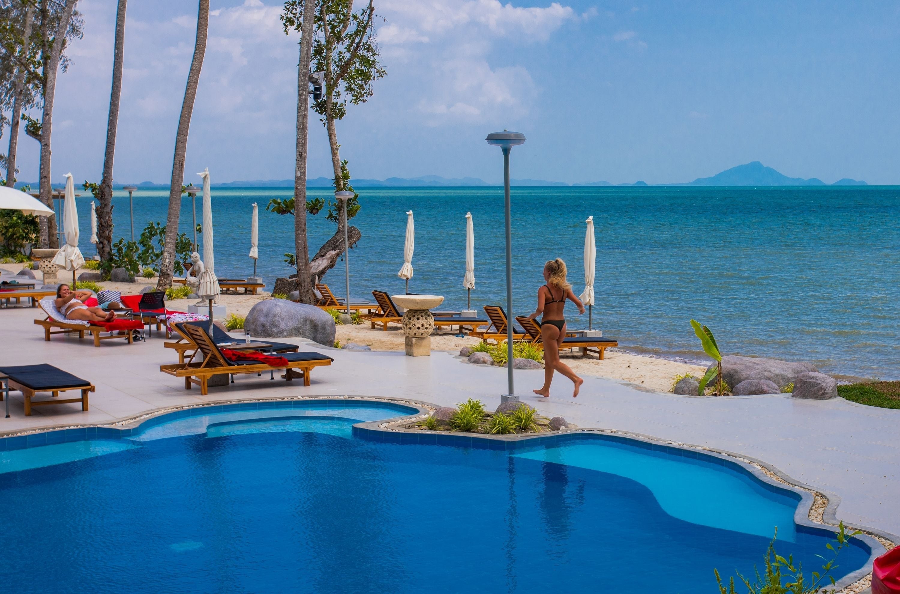 A poolside area with lounge chairs, umbrellas, and a clear view of the ocean.