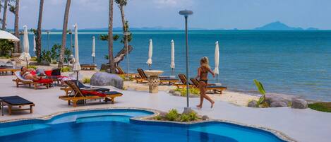 A poolside area with lounge chairs, umbrellas, and a clear view of the ocean.