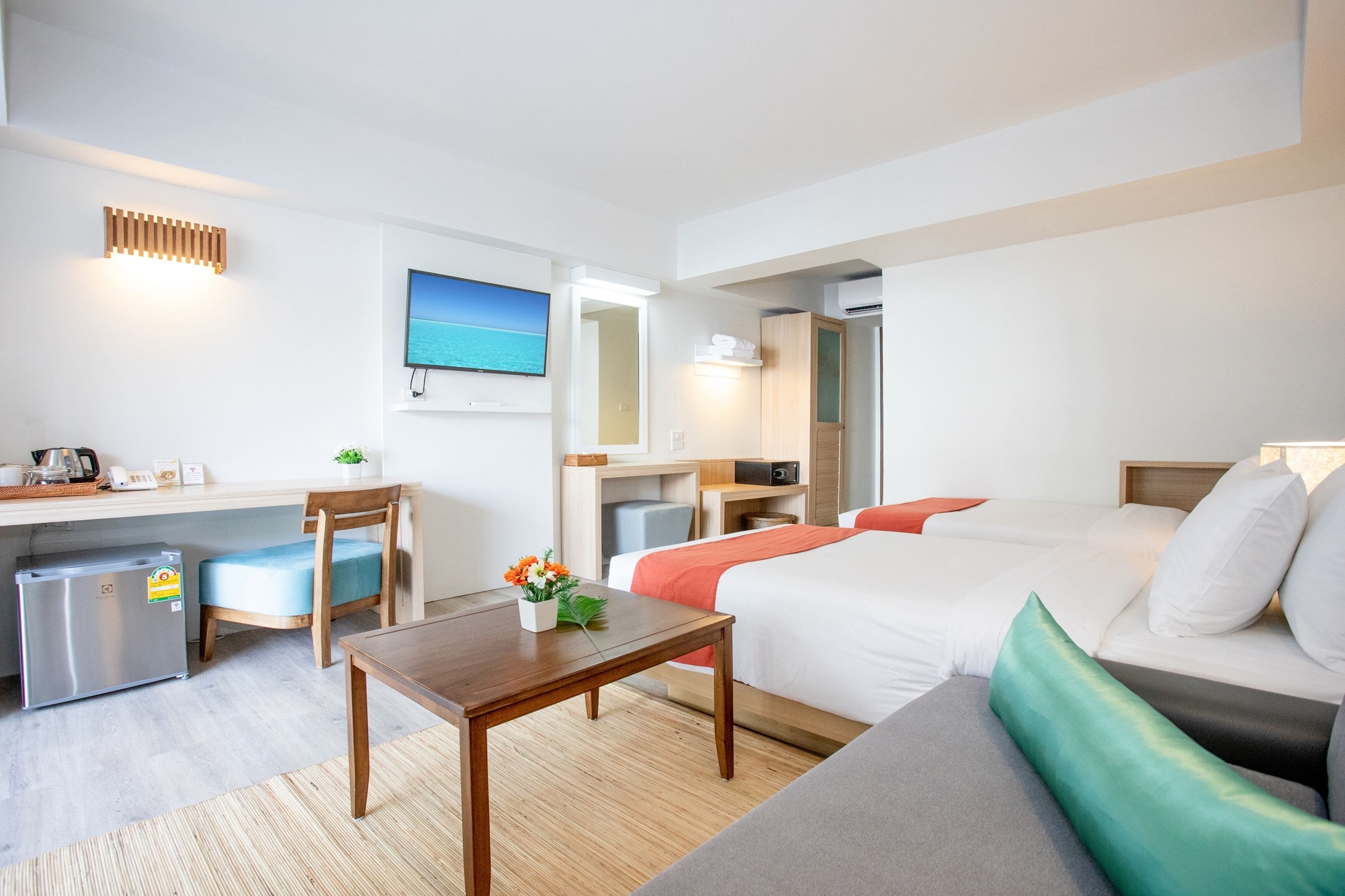 A hotel room with a bed, a desk, a chair, a small refrigerator, a TV, and a window with a view of the sea.