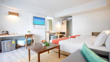 A hotel room with a bed, a desk, a chair, a small refrigerator, a TV, and a window with a view of the sea.